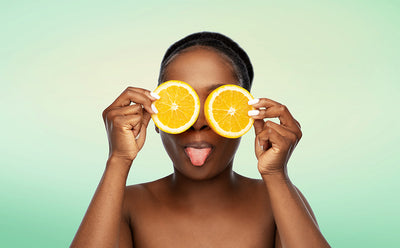 A black lady holding two orange slices in front of her eyes