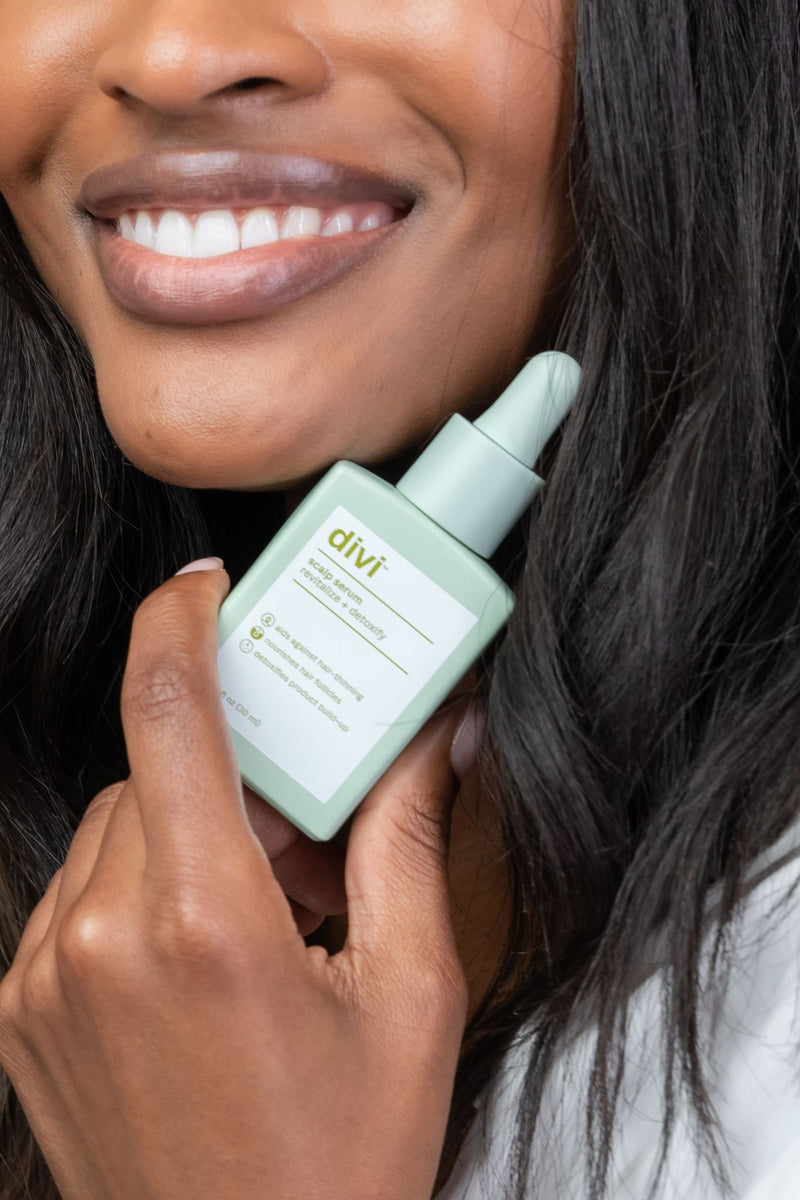 A lady smiling while holding a bottle of Divi's Scalp Serum